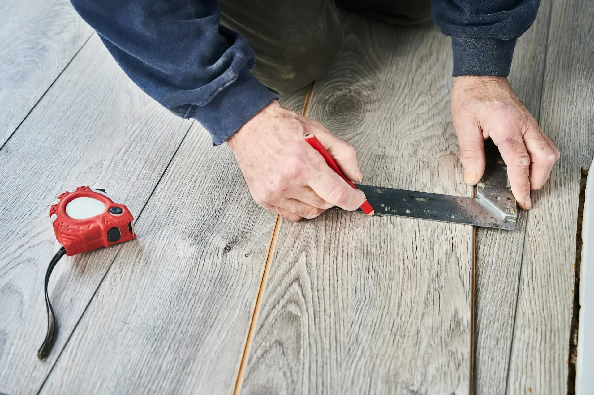 Male hands drawing line on laminate timber plank.